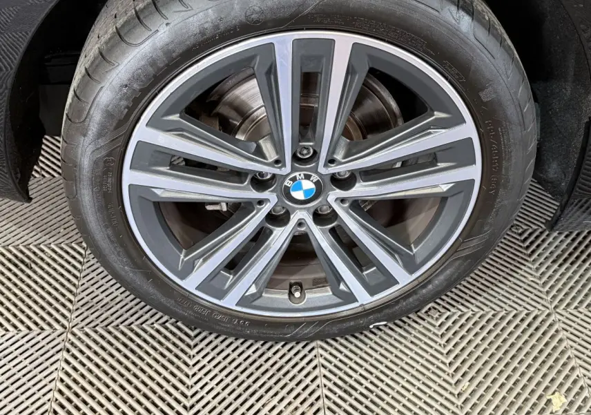 Gros plan sur la jante alliage grise avec logo BMW au centre, roue avant droite d'une BMW Série 1 noire.