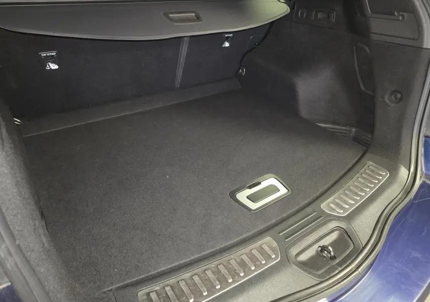 Coffre ouvert du Renault Koleos bleu, vue intérieure montrant le tapis noir et la trappe de rangement au sol.