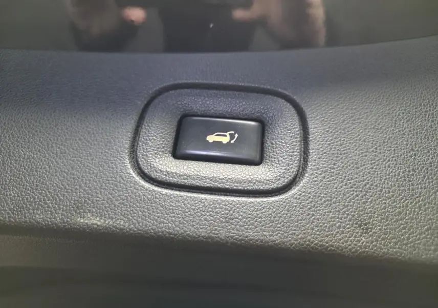 Bouton noir d'ouverture motorisée du hayon sur tableau de bord du Renault Koleos bleu de 2017, vue rapprochée.