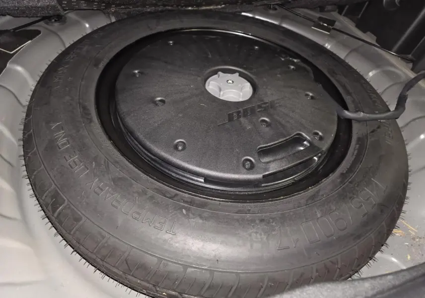 Gros plan sur la roue de secours galette noire avec caisson Bose intégré dans le coffre du Renault Koleos bleu.