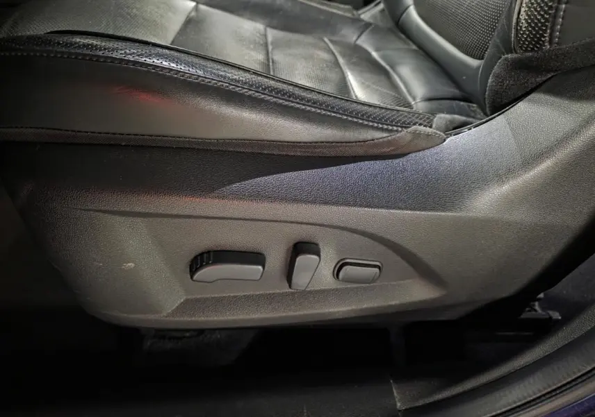 Gros plan sur les commandes électriques du siège avant gauche en cuir noir du Renault Koleos bleu de 2017.