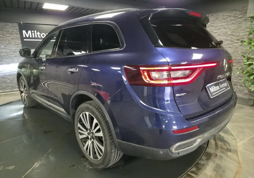 Vue 3/4 arrière droite du Renault Koleos bleu, avec feux arrière allumés et jantes alliage distinctives.