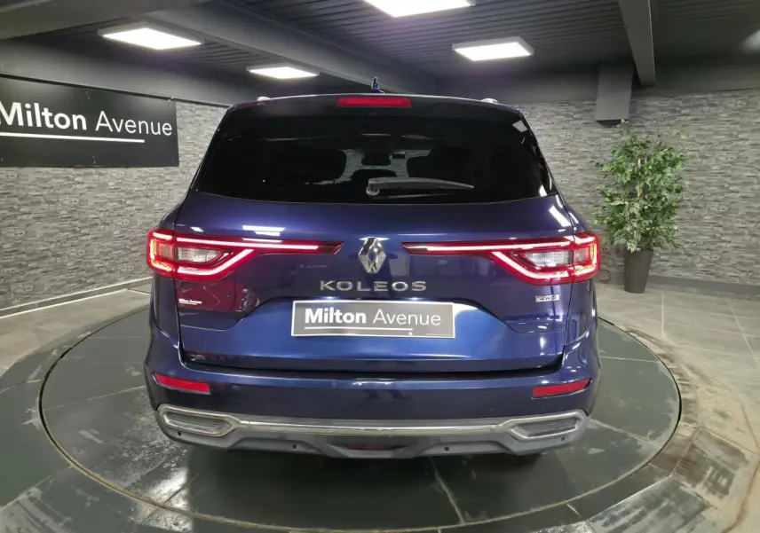 Vue arrière du Renault Koleos bleu de Saxe avec feux LED allumés et logo 4WD visible en intérieur showroom.