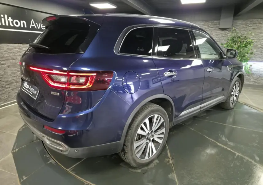 Vue 3/4 arrière droite du Renault Koleos bleu avec jantes alliage et vitres teintées dans un showroom.