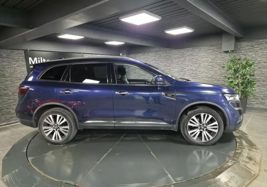 Profil droit du Renault Koleos bleu de Saxe 2017 avec jantes alliage et vitres teintées en intérieur showroom.