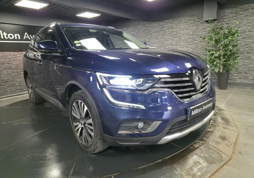Renault Koleos bleu de Saxe en 3/4 avant droit, feux LED allumés et calandre chromée Initiale Paris visible.