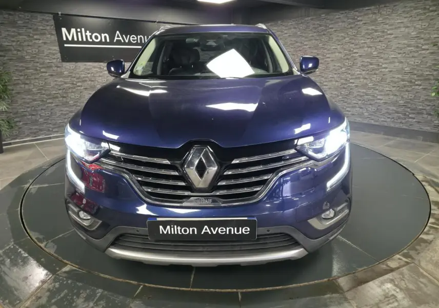 Vue frontale d'un Renault Koleos bleu avec calandre chromée et feux LED allumés en intérieur showroom.