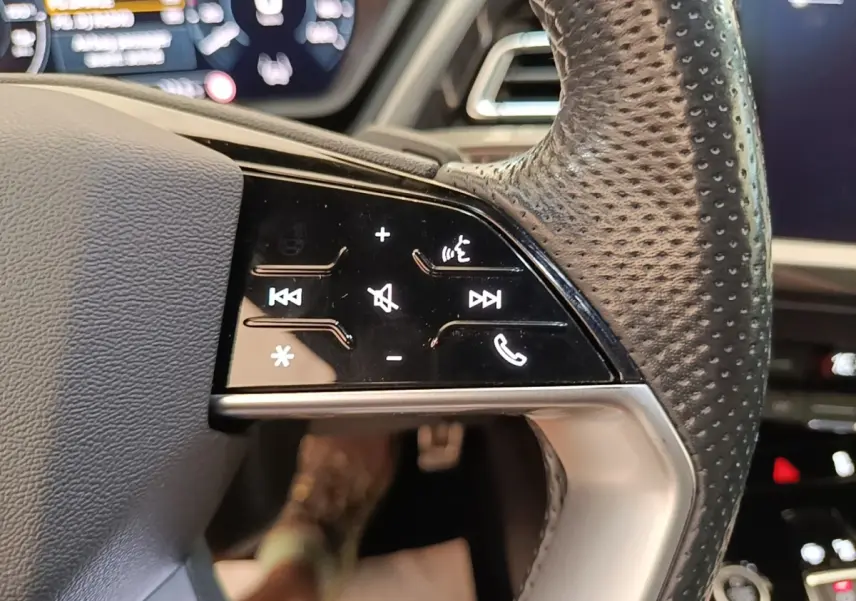 Gros plan sur le volant cuir perforé de l'Audi Q4 E-TRON Sportback, avec commandes tactiles noires et affichage numérique en arrière-plan.