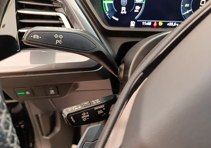 Gros plan sur les commandes au volant côté gauche de l’Audi Q4 E-TRON Sportback noir, avec affichage numérique en arrière-plan.