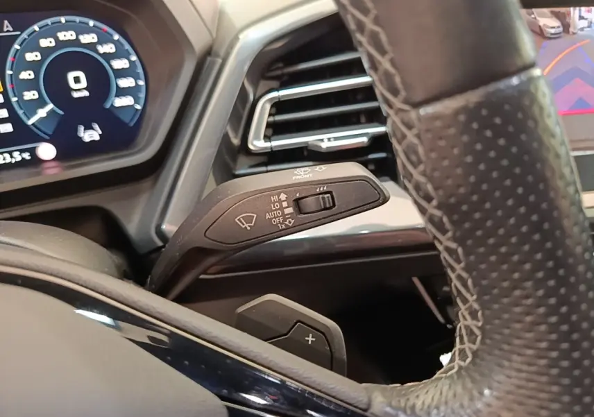 Gros plan sur le volant cuir et levier de commande des essuie-glaces de l'Audi Q4 E-Tron Sportback noir, tableau de bord numérique visible.