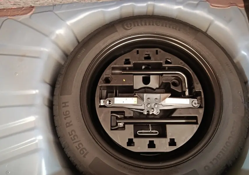 Gros plan sur la roue de secours et son kit d'outils dans le coffre d'une Renault Clio bleu 2026.
