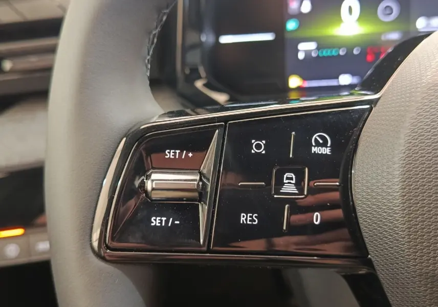 Gros plan sur les commandes multifonctions noires du volant réglable de la Renault Clio bleu, affichage numérique en arrière-plan.