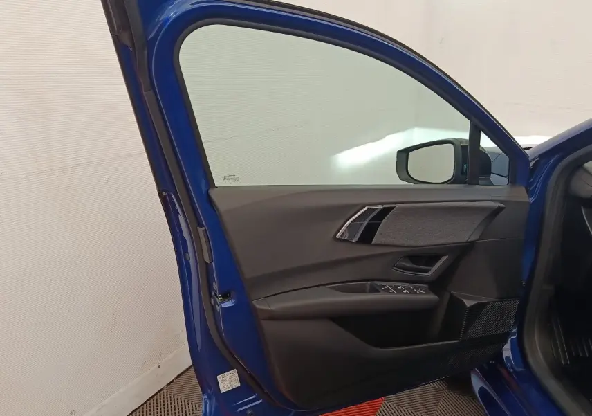 Portière avant gauche ouverte d'une Renault Clio bleu 2026, montrant les commandes de vitre et le rétroviseur intérieur.