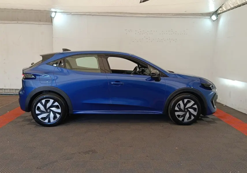 Profil droit d'une Renault Clio bleu 2026 avec jantes stylisées et toit noir dans un espace intérieur éclairé.