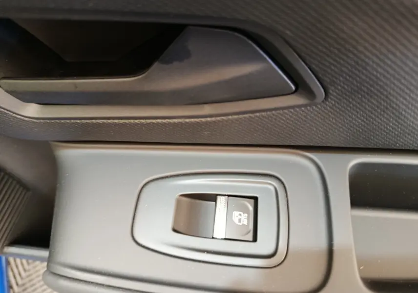 Gros plan sur le bouton de commande de la fenêtre électrique côté conducteur dans l’habitacle de la Renault Clio bleu.