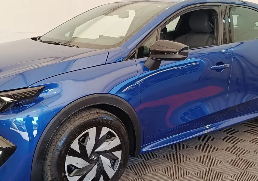 Vue de profil côté gauche d'une Renault Clio bleu métallisé avec jante au design géométrique et rétroviseur noir brillant.