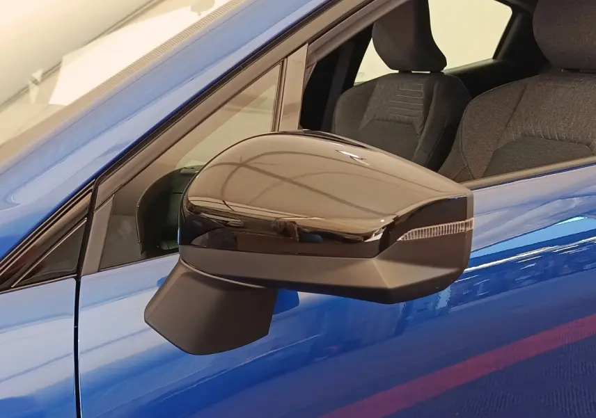 Gros plan sur le rétroviseur droit noir brillant d’une Renault Clio bleu intense, avec intérieur tissu visible.