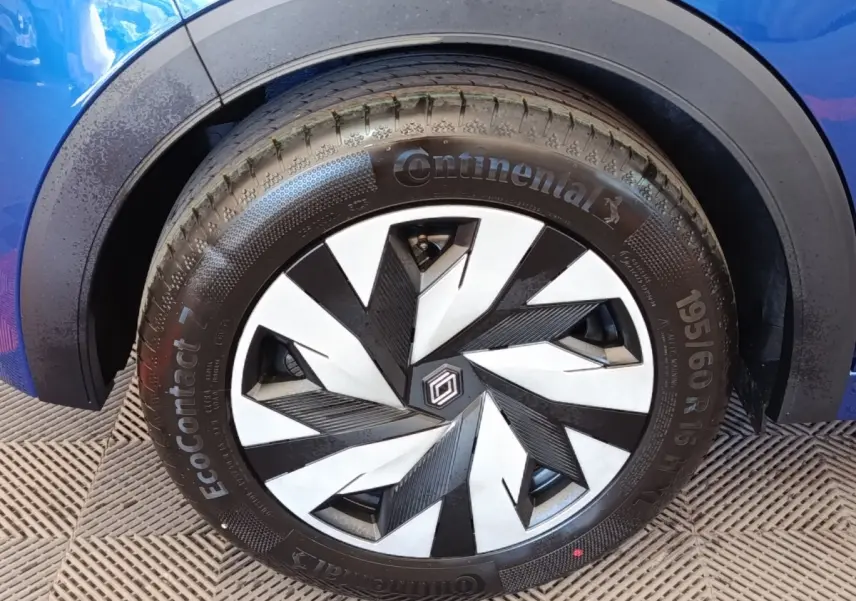 Gros plan sur la roue avant droite d’une Renault Clio bleue avec jante au design géométrique noir et argent.