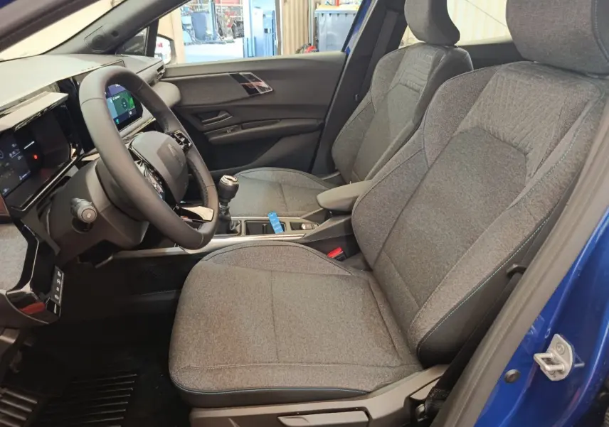 Intérieur côté conducteur de la Renault Clio bleu 2026, montrant sièges gris et volant multifonctions avec boîte manuelle.