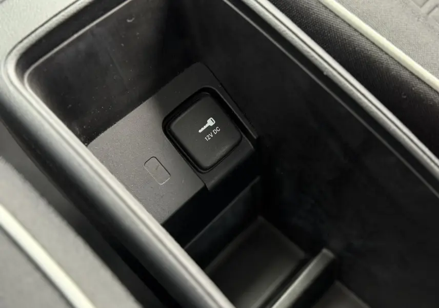 Prise 12V dans le rangement central intérieur de la Fiat 500 électrique blanche, vue en plongée rapprochée.