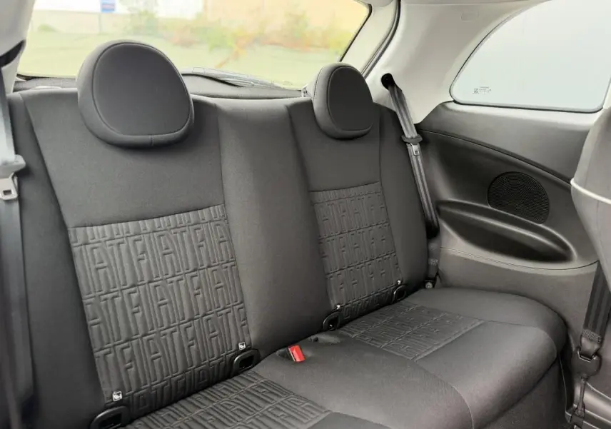 Vue intérieure arrière des sièges noirs avec motifs FIAT embossés sur la banquette d'une Fiat 500 électrique blanche.