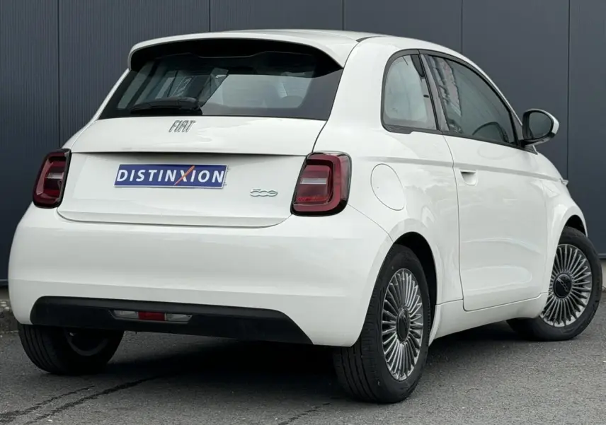 Vue 3/4 arrière droite d'une Fiat 500 électrique blanche avec feux arrière sombres et jantes stylisées.
