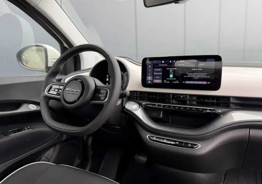 Intérieur de la Fiat 500 électrique 2023, vue côté conducteur, tableau de bord blanc avec écran tactile central et volant noir.