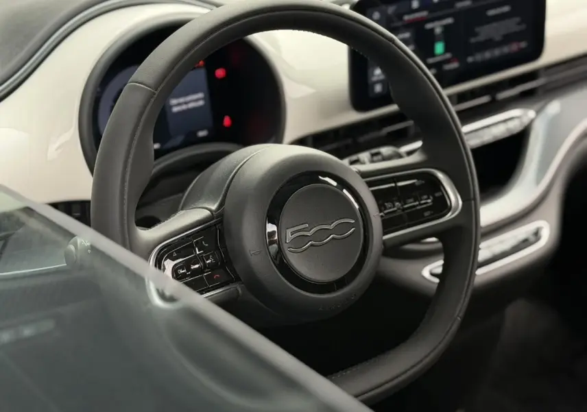 Vue rapprochée du volant noir et du tableau de bord blanc de la Fiat 500 électrique 2023 avec commandes intégrées.