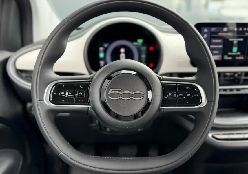 Vue centrée sur le volant noir de la FIAT 500 électrique 2023 avec tableau de bord numérique et écran tactile.