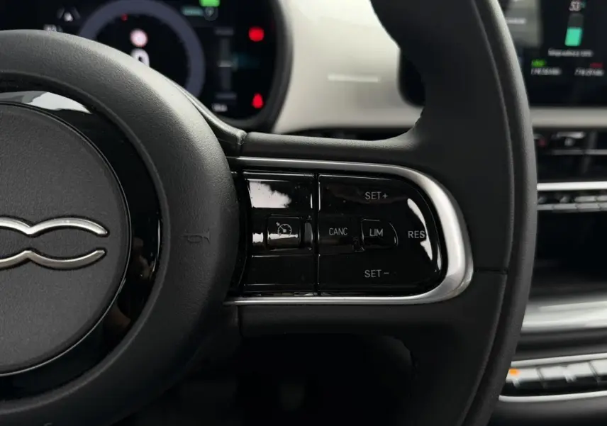 Gros plan sur le côté droit du volant noir de la FIAT 500 électrique blanche, avec commandes de régulateur de vitesse.