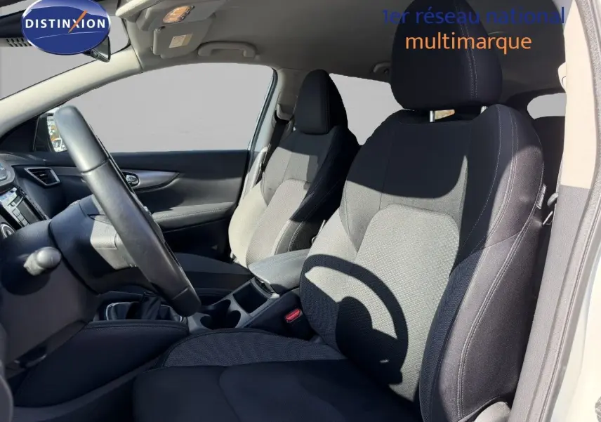 Vue intérieure côté conducteur du Nissan Qashqai blanc nacré, montrant les sièges avant en tissu noir et gris.