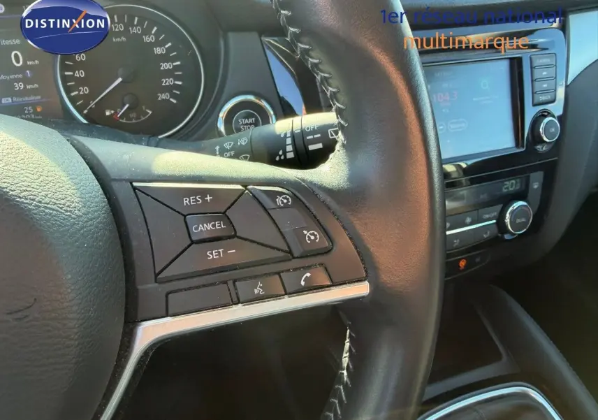 Gros plan sur le volant et le tableau de bord du Nissan Qashqai blanc nacré, avec commandes au volant et écran tactile visible.