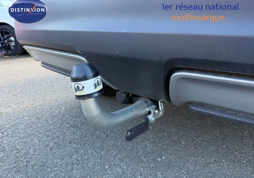 Gros plan sur l'attelage arrière d'un Nissan Qashqai blanc nacré, avec pare-chocs noir et sol goudronné visible.
