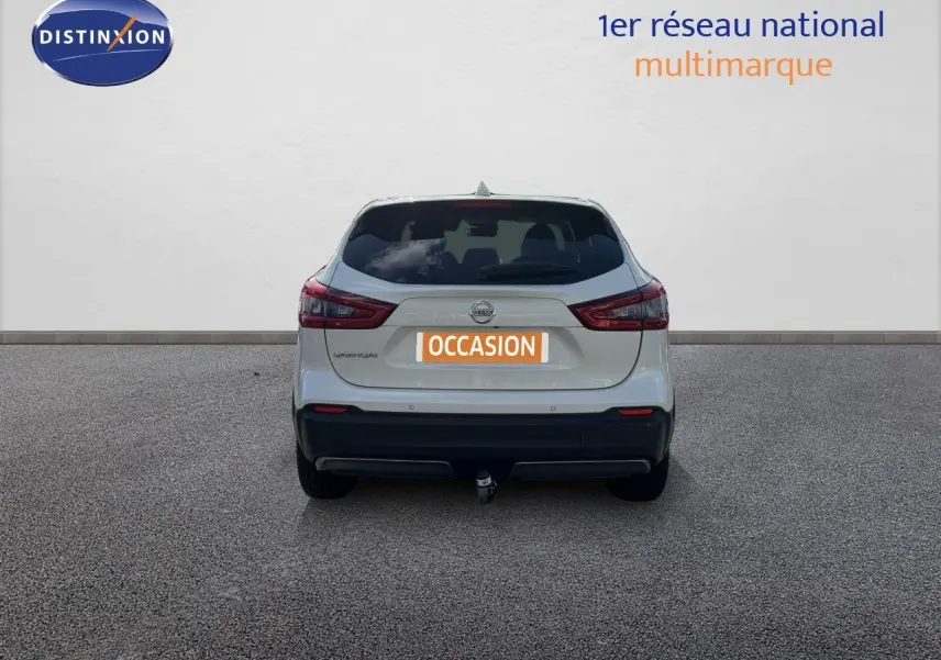 Vue arrière d'un Nissan Qashqai blanc nacré métal 2019 avec attelage et feux arrière allumés.