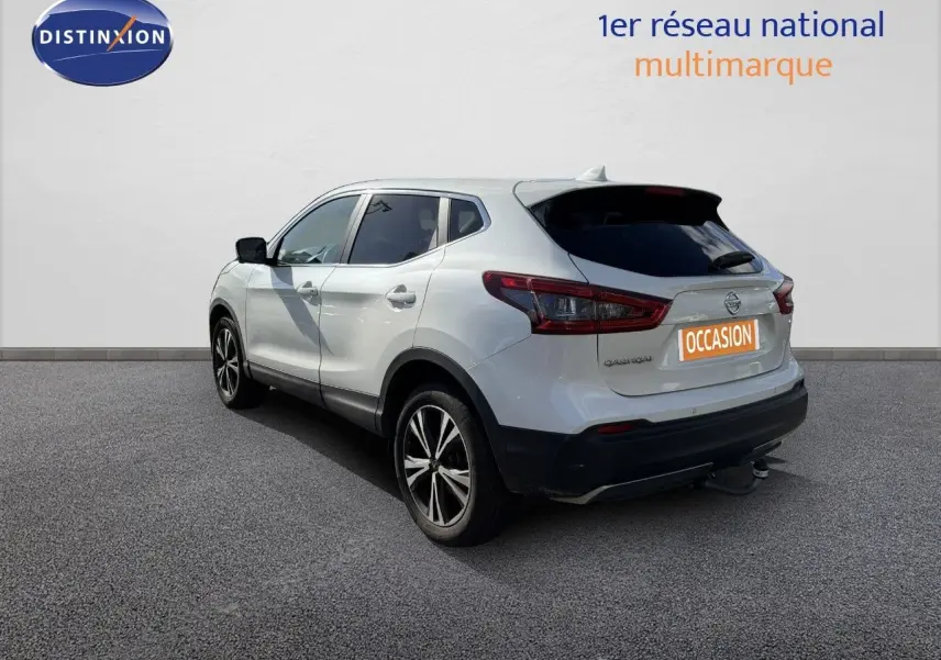 Vue 3/4 arrière droite du Nissan Qashqai blanc nacré avec jantes alliage et attelage visible sur fond neutre.