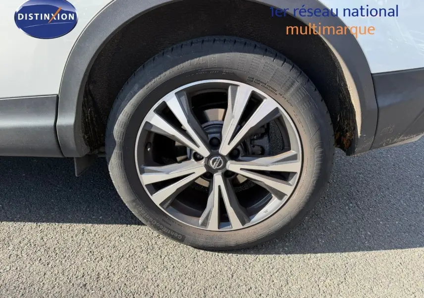 Gros plan sur la roue avant droite d’un Nissan Qashqai blanc nacré avec jante alliage à design moderne.