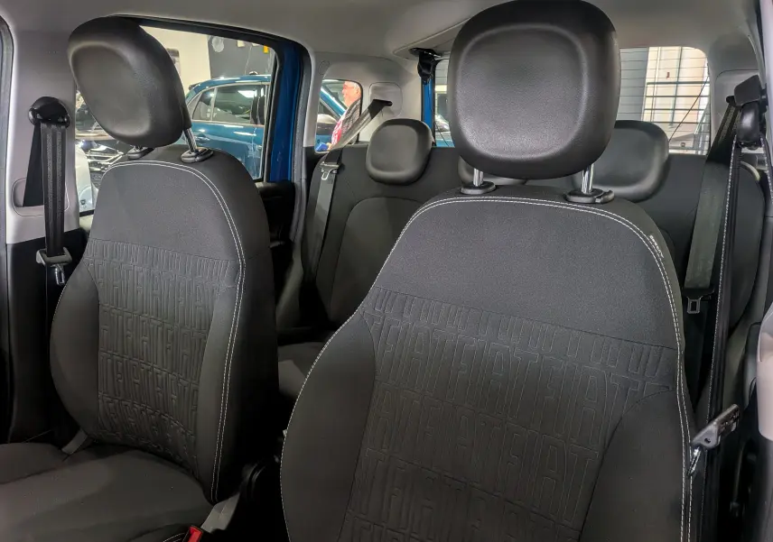 Intérieur de la Fiat Panda 2025 en Bleu Italia, vue des sièges avant en tissu noir avec motifs FIAT embossés.