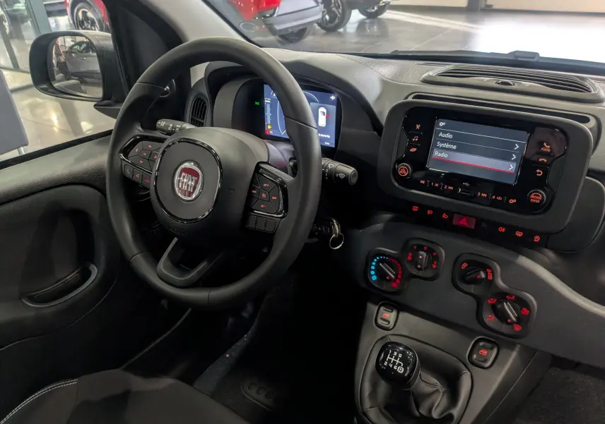 Intérieur de la Fiat Panda 1.0 Hybrid 2025 vu côté conducteur, tableau de bord avec écran tactile et commandes manuelles.