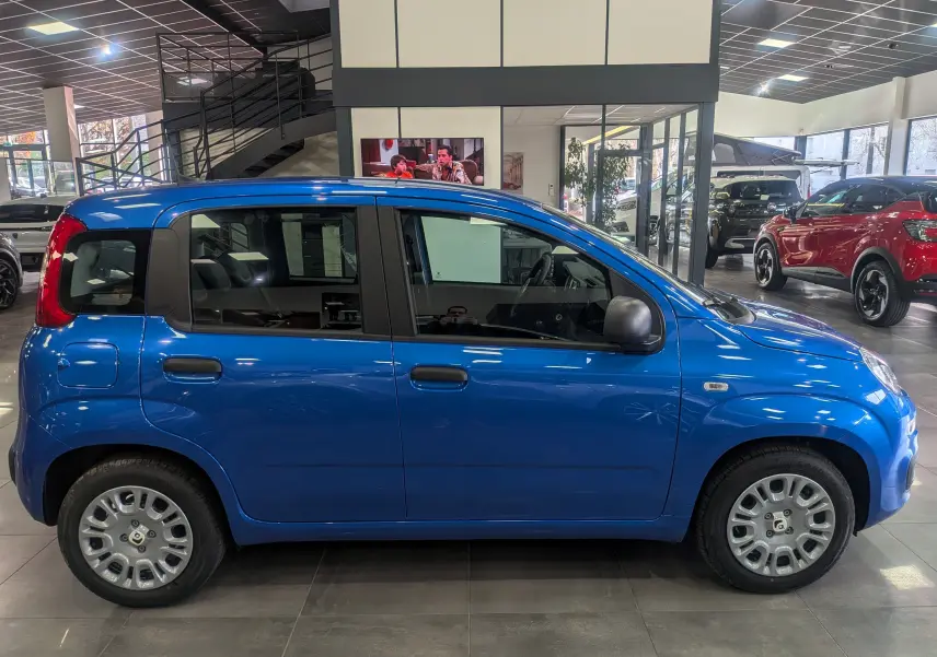 Profil côté droit de la Fiat Panda 1.0 Hybrid City 2025 en Bleu Italia, compacte et pratique en intérieur de showroom.