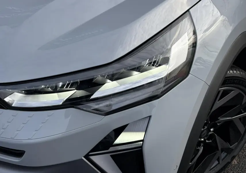Gros plan sur le phare avant droit du Renault Captur gris Rafale avec jante noire et détails anguleux modernes.