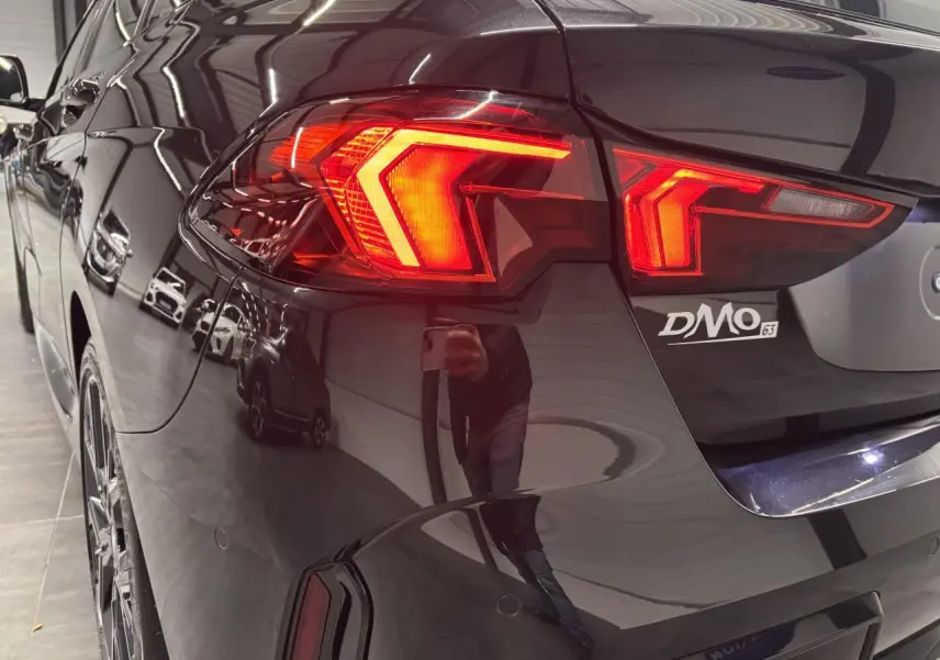 Vue arrière côté gauche d'une BMW Série 1 118d M Sport noire métal avec feux arrière LED allumés.