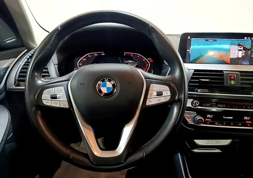 Vue intérieure centrée sur le volant cuir noir et le tableau de bord digital du BMW X3 sDrive18d 2019.