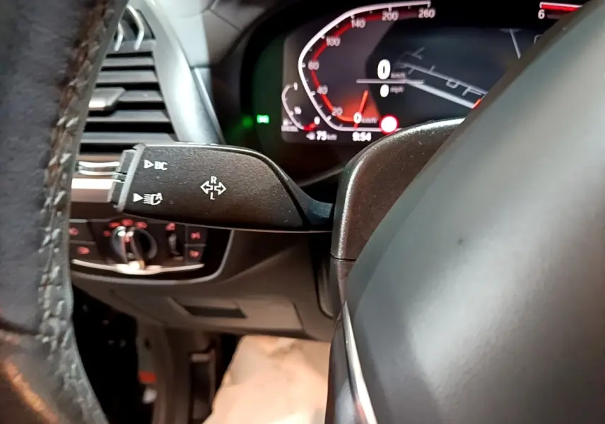 Gros plan sur la manette de clignotants et le tableau de bord numérique du BMW X3 noir, intérieur côté conducteur.