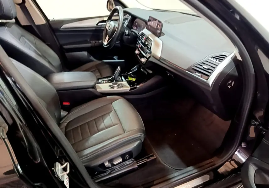 Vue intérieure côté conducteur du BMW X3 noir 2019, montrant sièges cuir et tableau de bord avec écran tactile.