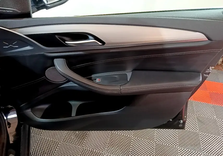 Gros plan sur la porte intérieure côté gauche d’une BMW X3 noire, avec garniture cuir et insert décoratif clair.