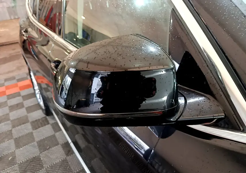 Rétroviseur côté gauche noir brillant avec gouttes d'eau sur BMW X3 sDrive18d Luxury 2019, vue rapprochée en angle.