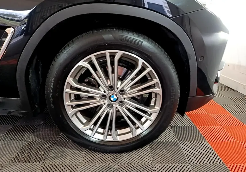 Gros plan sur la roue avant droite d’un BMW X3 noir, mettant en valeur la jante alliage multi-branches et le pneu Pirelli.