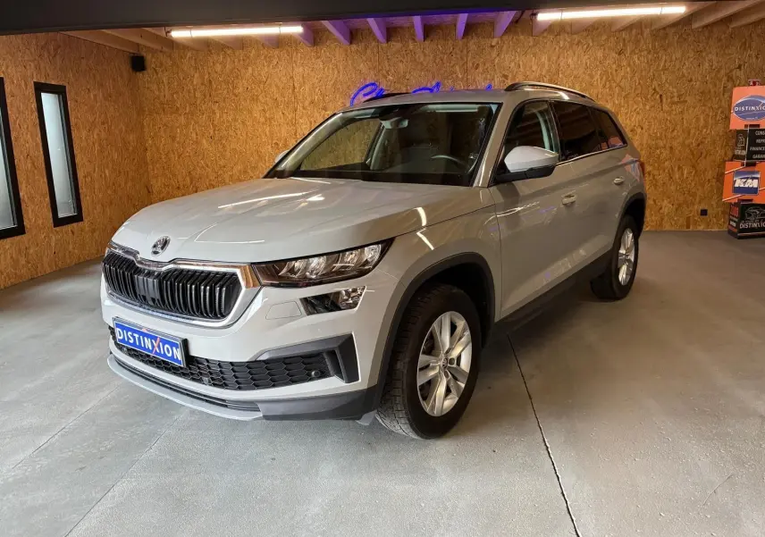 Vue 3/4 avant droite d'un Skoda Kodiaq gris clair 2023 en intérieur avec calandre noire et jantes argentées.