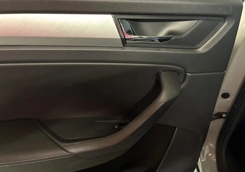 Vue rapprochée de la porte intérieure côté droit d’un Skoda Kodiaq gris clair 2023, avec poignée noire et insert métal brossé.