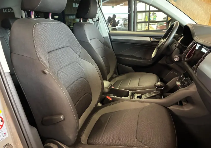 Vue intérieure côté gauche du Skoda Kodiaq 2023 gris clair, montrant les sièges avant en tissu noir et le tableau de bord.
